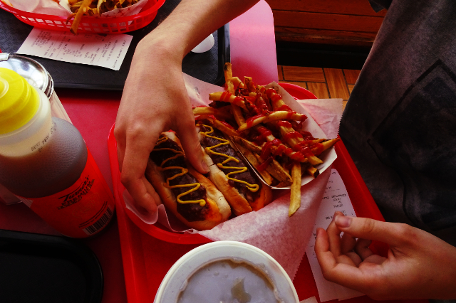A hand reaching down to pick up one of two chili dogs dressed in zig-zagging mustard trails