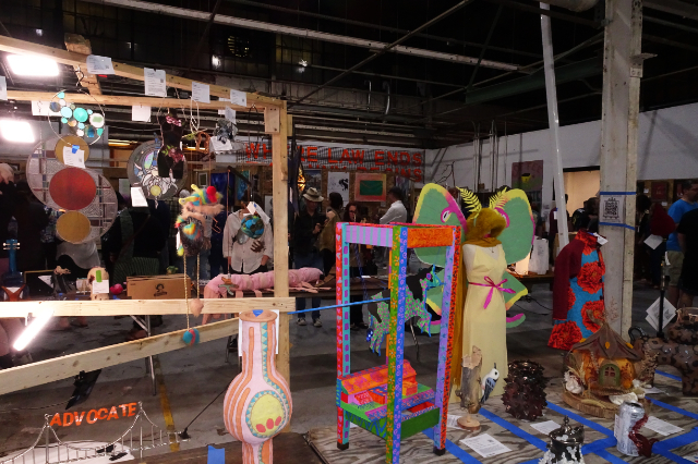 A view of the space, showing brightly colored and bizarre objects on tables and walls as far as the eye can see.